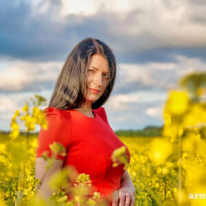 Ilgaplaukė mergina raudona suknele geltonų gėlių pievoje