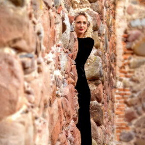 Moteris ilga juoda suknele prie akmeninės sienos